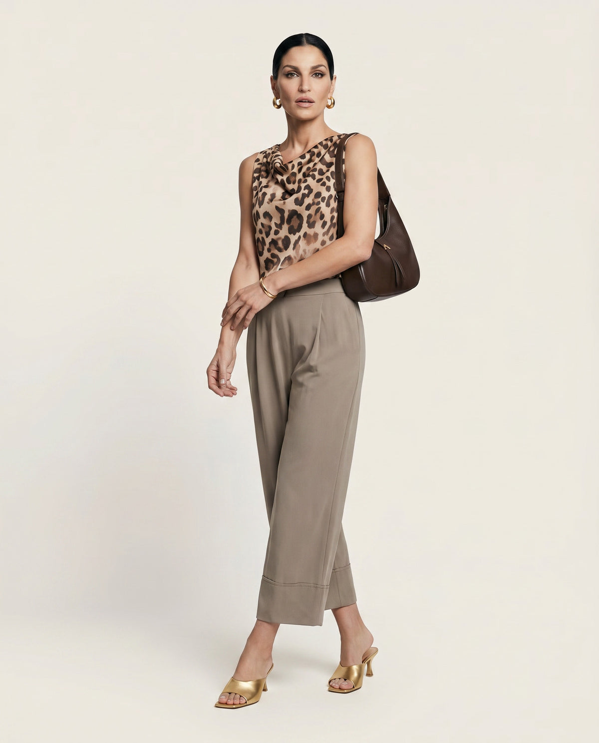 Woman wearing a leopard print top and beige pants with a brown handbag on a light background